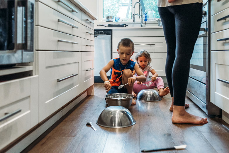 Boy and girl make noise with metal bowls in the kitchen