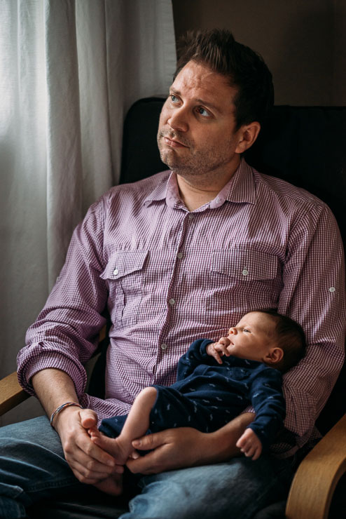 Father holding newborn son and looking out the window