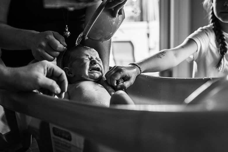 Big sister's hand holding newborn brother's hand at bath time