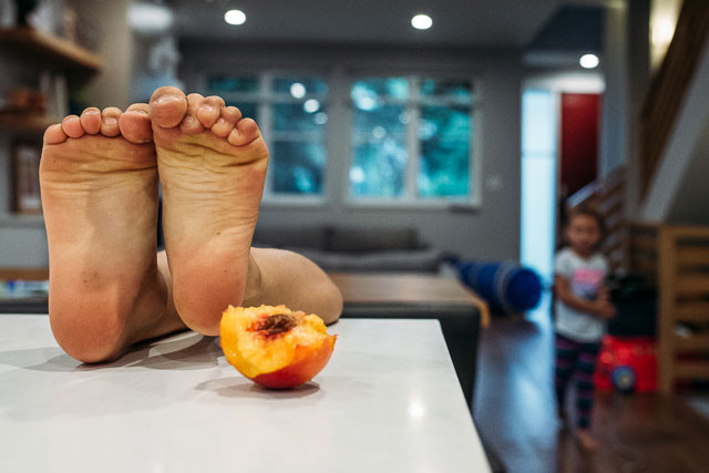 Boy's feet on countertop next to half eaten peach
